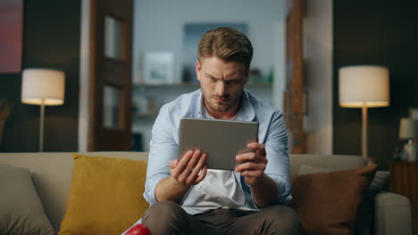 Focused hipster examining tab computer sitting couch. Man zooming pad screen