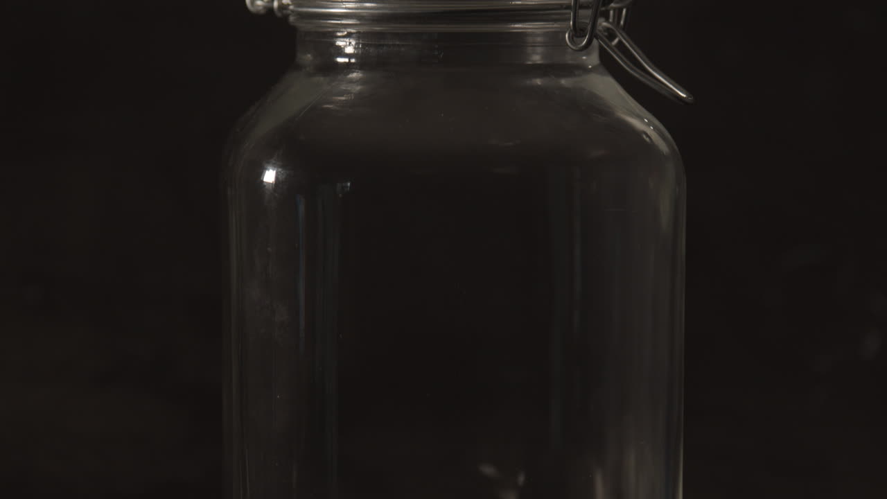 Tilt up of glass preserving jar with metal bracket against a black background