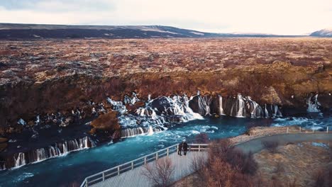 Drohne-Mit-Filmischen-Bewegungen-Zeigt-Den-Wunderschönen-Isländischen-Wasserfall-Hraunfossar-Im-Sonnenuntergangslicht-Aus-Mehreren-Winkeln