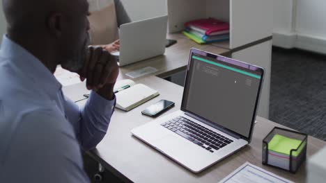 hombre afroamericano sentado en el escritorio viendo el procesamiento de datos de codificación en la pantalla del portátil