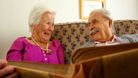 vista frontal de una pareja de ancianos caucásicos activos mirando un álbum de fotos en un hogar de ancianos 4k