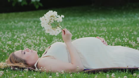 Cute-Pregnant-Woman-Lies-On-A-Lawn-Holds-A-Flor-In-Her-Hand-Dreams