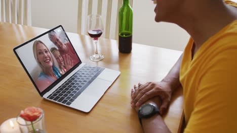 Mid-section-of-african-american-man-talking-on-video-call-on-laptop-at-home