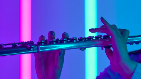 musical concert of classical music performed by a professional female flutist. female hands with a flute close up. wind instrument against the background of bright neon lights. slow motion