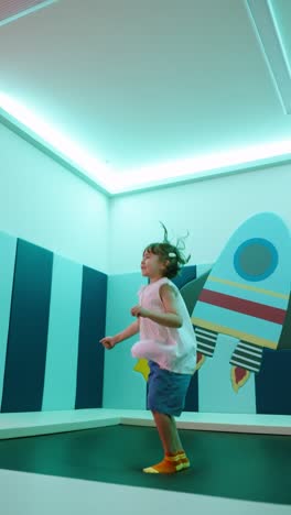 a cheerful young girl with dark hair and white top is happily jumping on a trampoline, doing a peace sign gesture and other poses while looking at the camera
