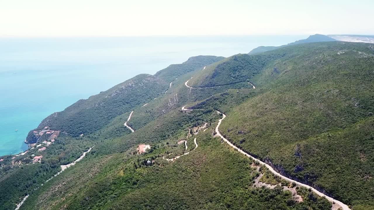 Aerial view of winding roads and lush green hillsides in Parque Natural da Arrábida, Portugal. The stunning coastal scenery offers a picturesque blend of natural beauty and serene landscapes