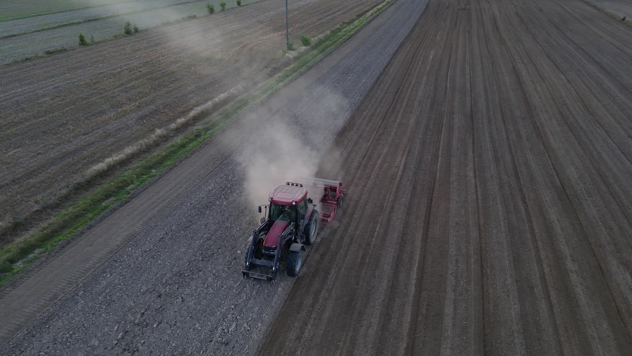 Evening drone shot of tractor cultivating soil at sunset. Dust trails rise as camera tilts down from horizon into golden farmland