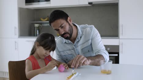 niña y su padre pintando huevo juntos