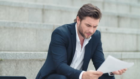 hombre de negocios examinando papeles de negocios al aire libre. gerente masculino sentado en las escaleras