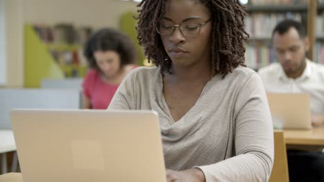 Estudiante-Pensativo-En-Anteojos-Usando-Un-Dispositivo-En-La-Biblioteca-Pública