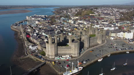 Eine-Luftaufnahme-Von-Caernarfon-Castle-An-Einem-Sonnigen-Tag,-Von-Rechts-Nach-Links-Um-Das-Schloss-Herumfliegend,-Gwynedd,-Nordwales,-Großbritannien