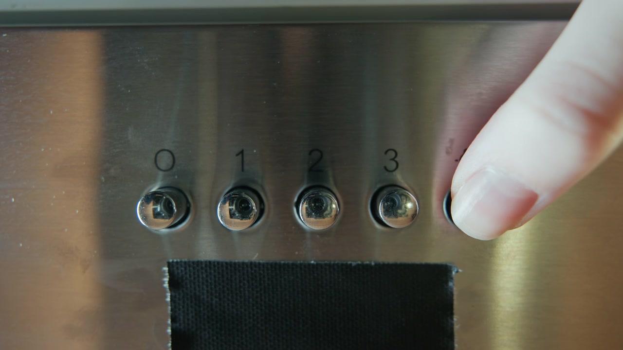 Close view of stainless steel control knobs on brushed metal appliance panel beside dark gasket opening, with hand pressing and turning controls in tactile functional use, with knob, finger, press