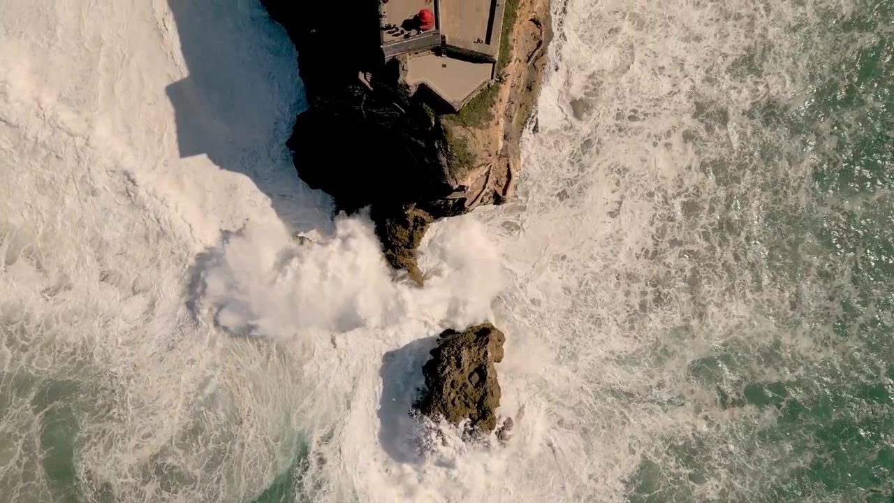 Vista dall'alto di onde enormi che si infrangono sulle rocce e sulle scogliere del Forte di São Miguel Arcanjo, Nazaré, Portogallo. - aerea.