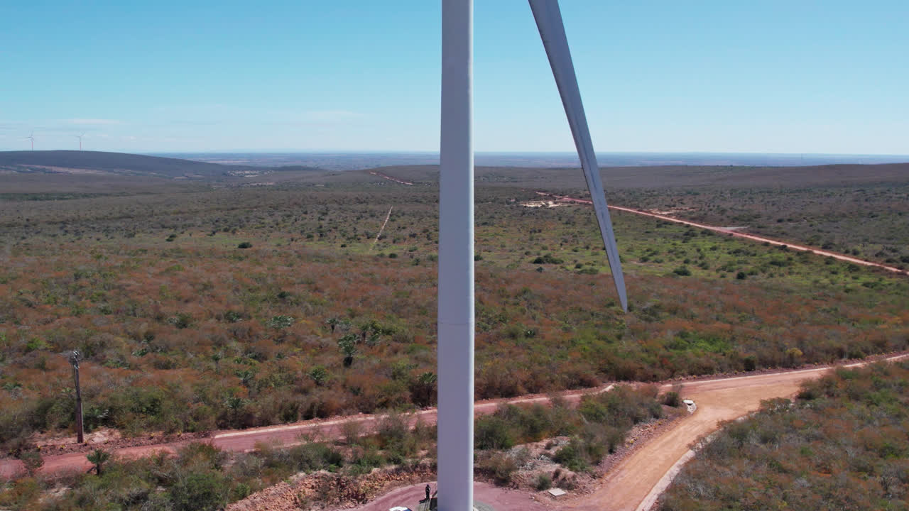 Tilt up aerial reveal of rotating wind turbine up close with car parked at the base and beautifull blue sky