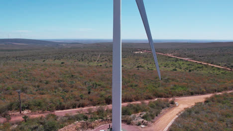 tilt up aerial reveal of rotating wind turbine up close with car parked at the base and beautifull blue sky
