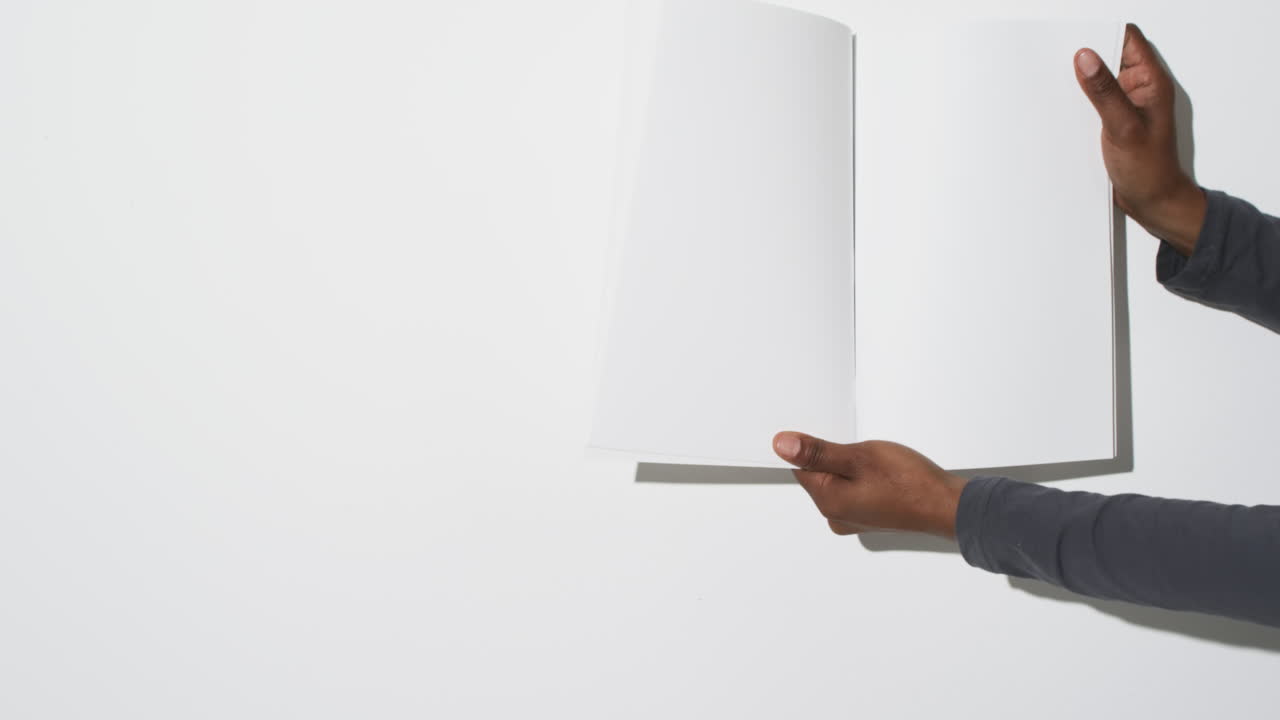 video de la mano de un hombre afroamericano sosteniendo un libro con páginas en blanco, espacio de copia en fondo blanco