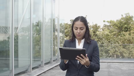Dolly-Shot-Of-A-Focused-Latin-Businesswoman-In-Suit-Using-Tablet-For-Work-While-Walking-Outside