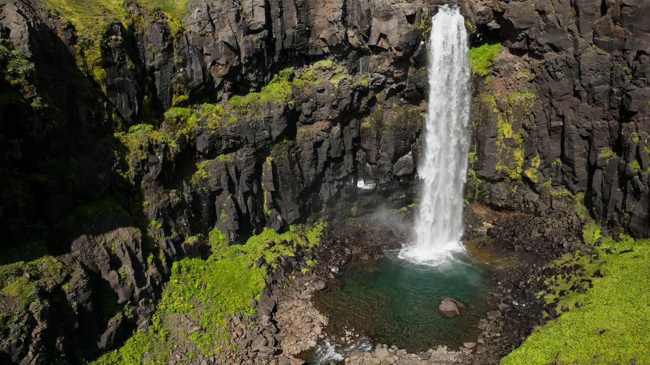cascada con agua clara que desemboca por un acantilado de piedra volcánica negra, vista aérea