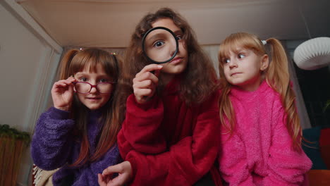 children sisters girls holding magnifying glass near face looking into camera analysing playing