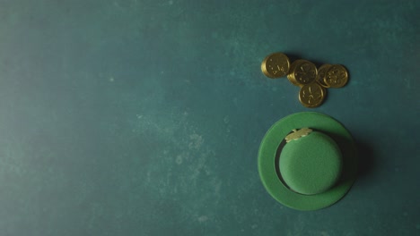 overhead studio shot of green leprechaun top hat and hand picking up gold coins to celebrate st patricks day