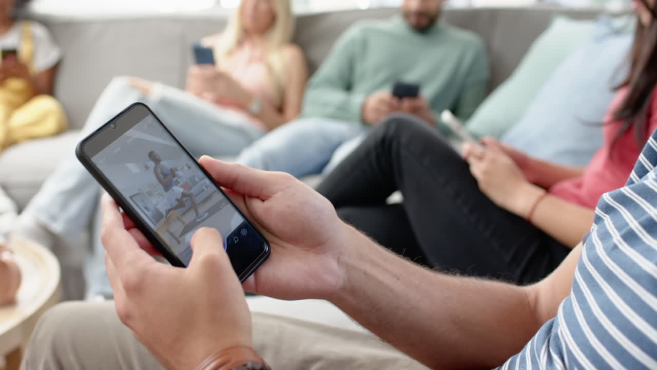 Using smartphone, young diverse friends relaxing on couch and browsing social media