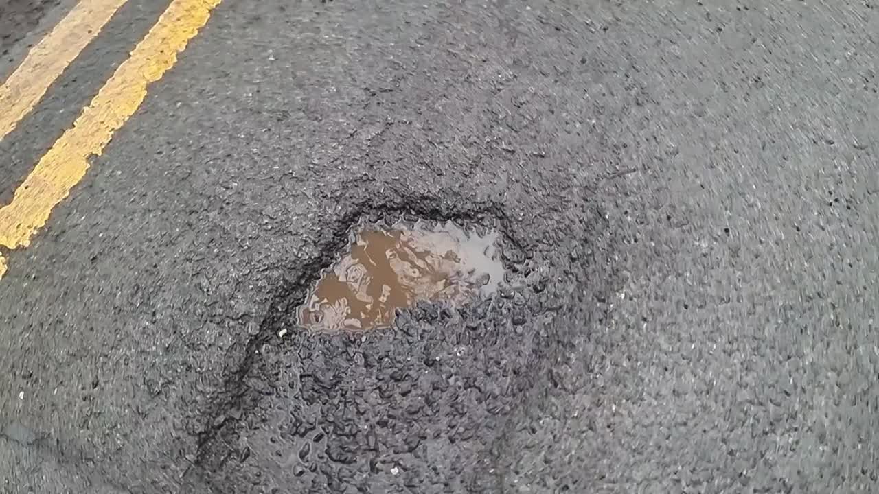 Road hazard double yellow lines with water filled pot hole damaged tarmac asphalt surface