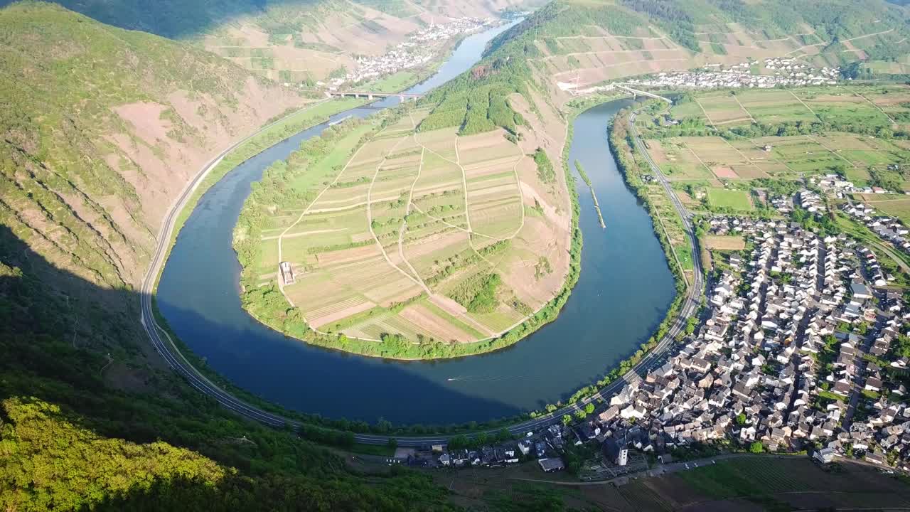 Khung cảnh trên không tuyệt đẹp của Moselschleife ở Đức, nổi bật với Sông Moselle uốn lượn, những vườn nho tươi tốt trên những ngọn đồi nhấp nhô và một ngôi làng gần đó nép mình dọc theo bờ sông dưới ánh sáng ban ngày.