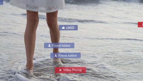 animation of social media notifications over legs of woman on holiday paddling in the sea