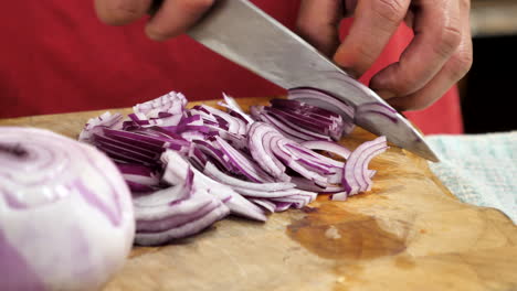 chef profesional prepara y corta cebolla roja en tabla de cortar de madera