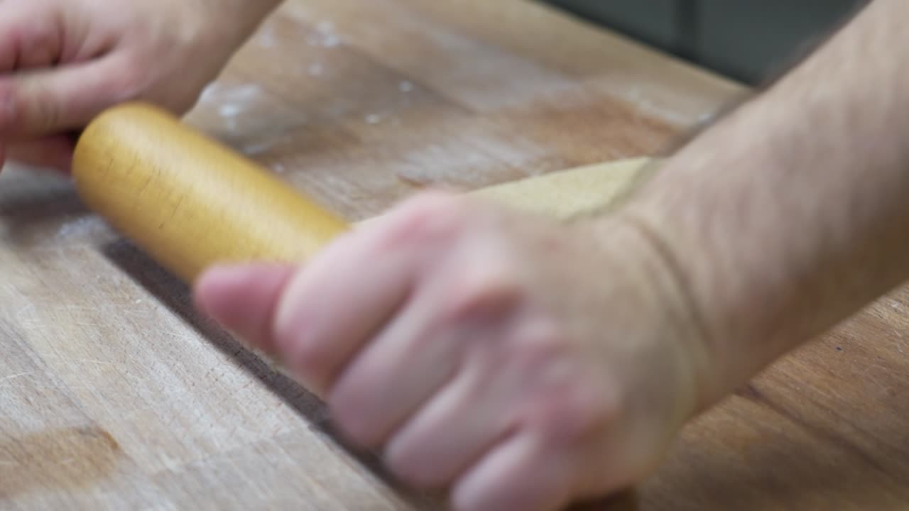 Hands rolling out Hungarian bejgli dough with a wooden rolling pin for Christmas baking