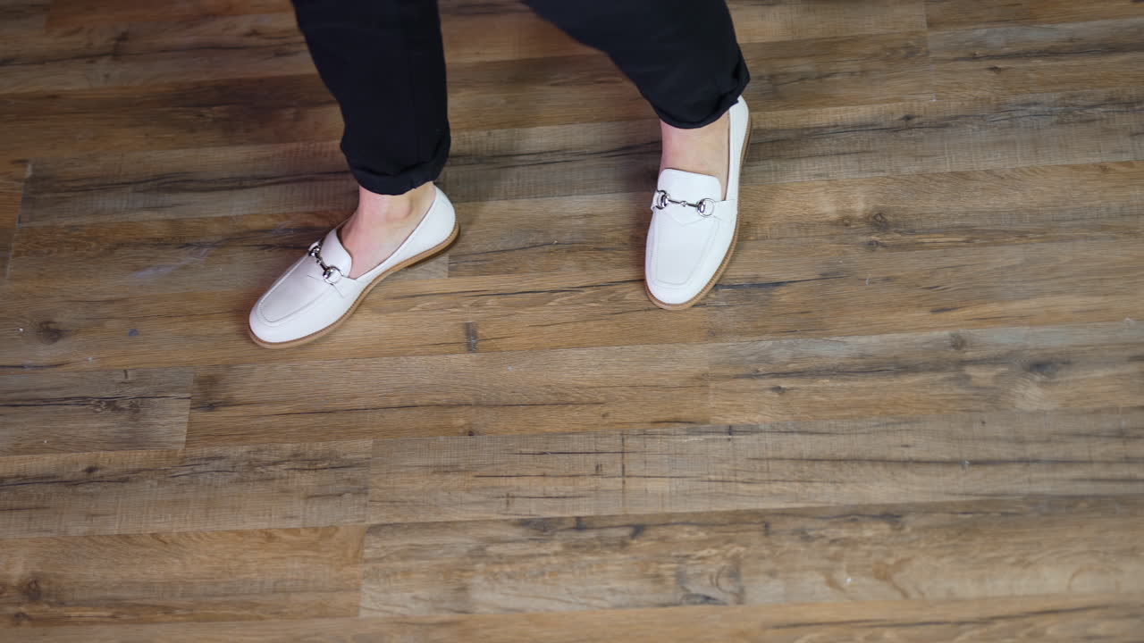 White comfortable casual shoes demonstration. Lady model posing in new footwear at the backdrop of wooden floor. View from top.