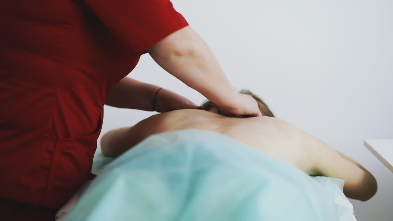 la terapeuta hace masaje del cuello enfermo del paciente en el sofá