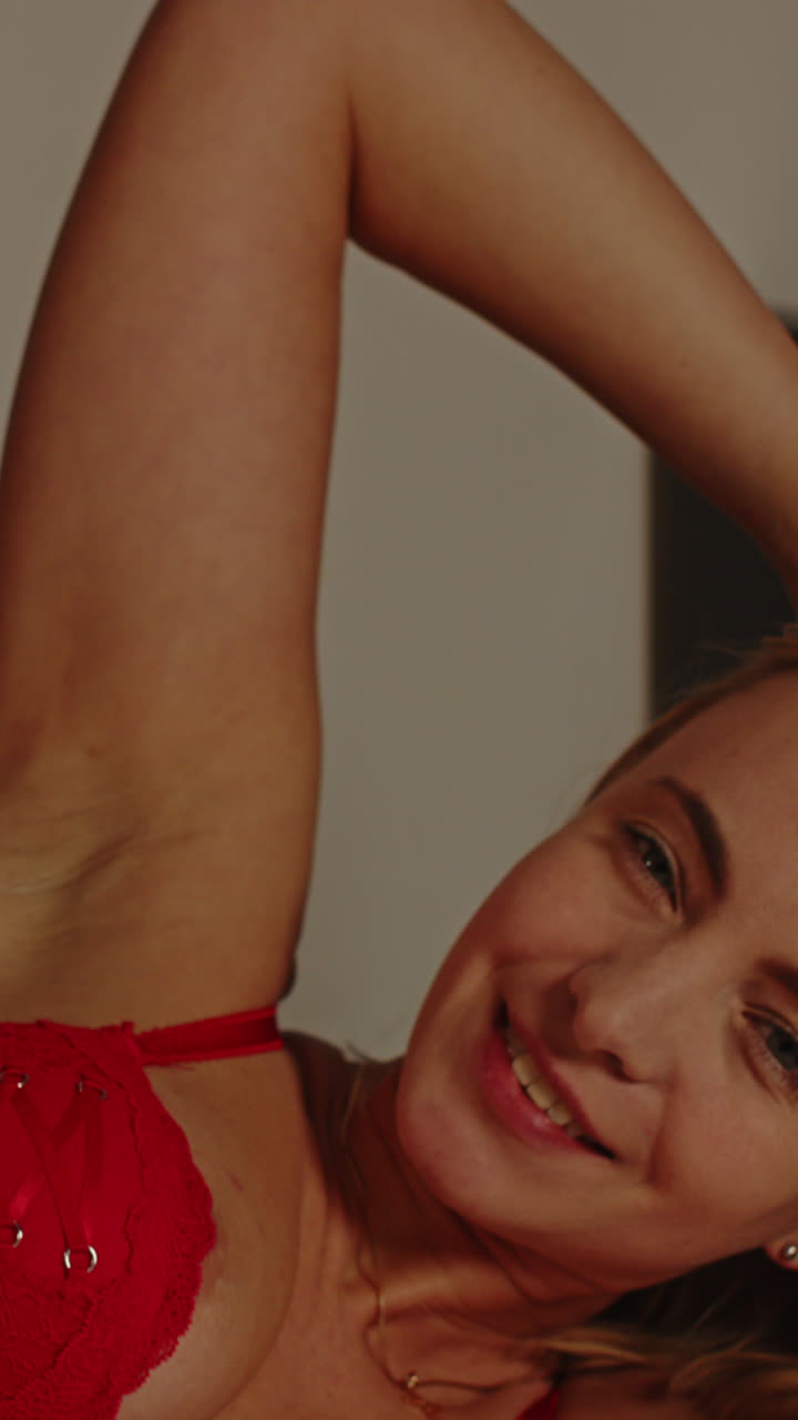 Primo piano verticale sensuale di una donna sensuale in lingerie rossa, sdraiata a letto e che guarda la fotocamera.