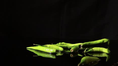 pimientos verdes de ojo de pájaro en cámara lenta que caen sobre una superficie de plato blanco con un charco de agua reluciente en verduras frescas picantes individuales para cocinar
