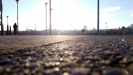 hooded person walking on early glowing sunrise city waterfront pavement low angle shot cityscape