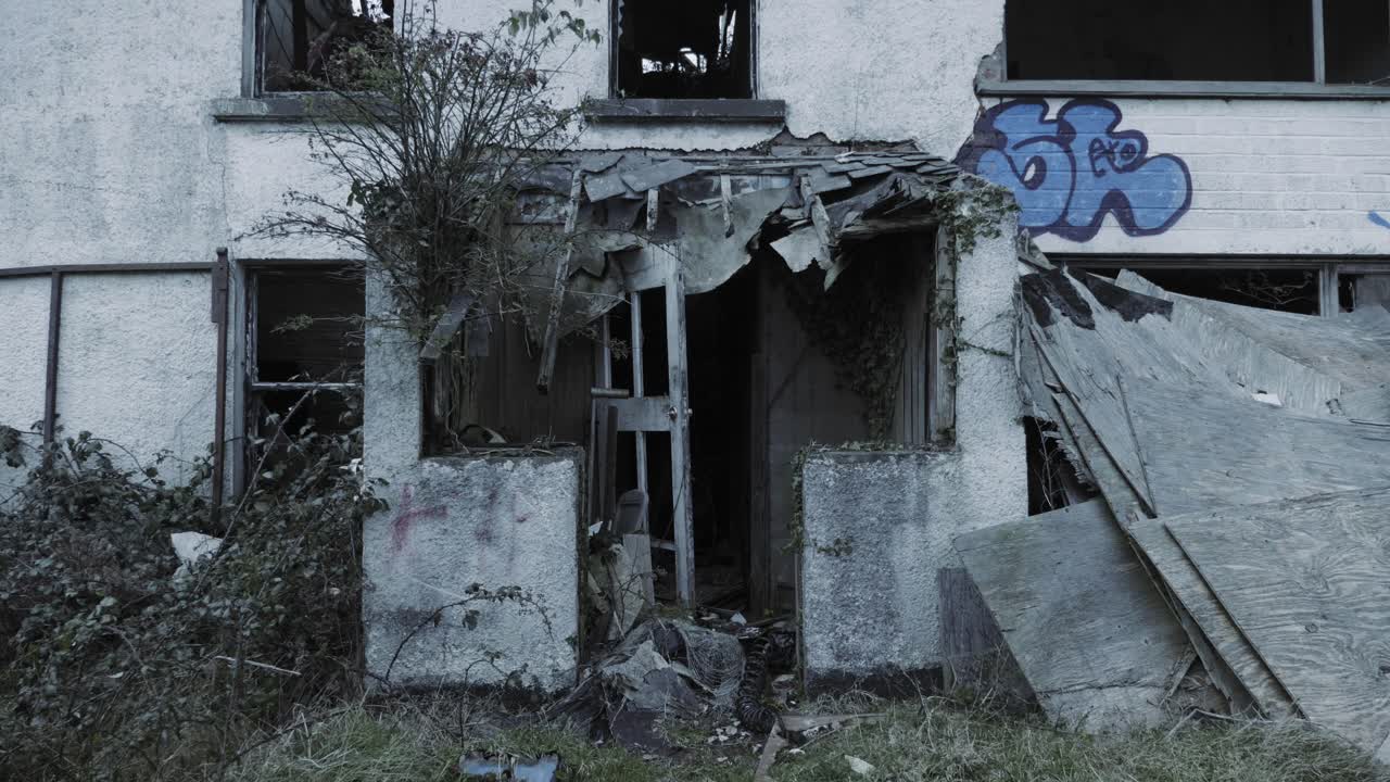 Overgrown Plants Inside The White Abandoned Building With A Grafitti And A Broken Gate In North Ireland. -medium shot