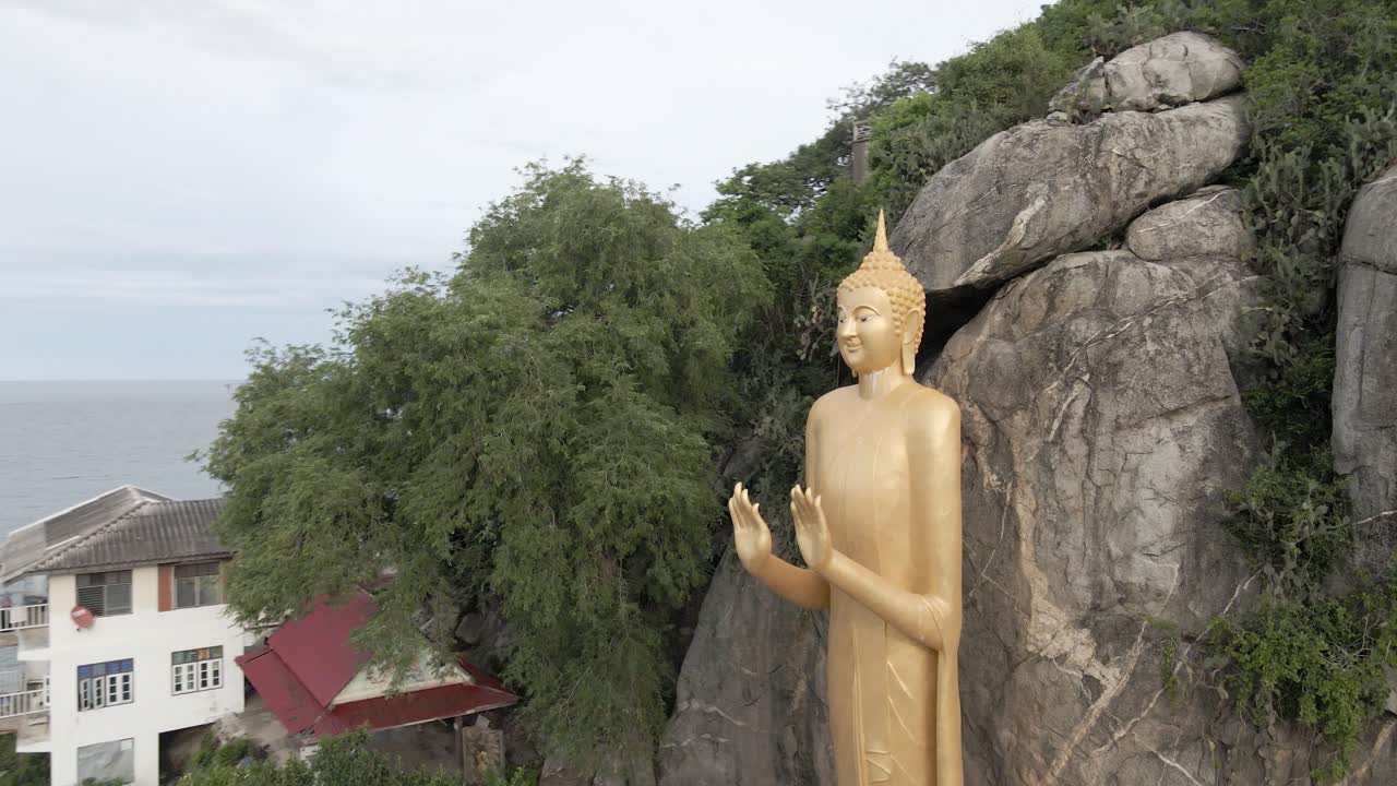 беспилотник пролетает по орбите рядом с гигантской золотой статуей будды на скале, таиланд