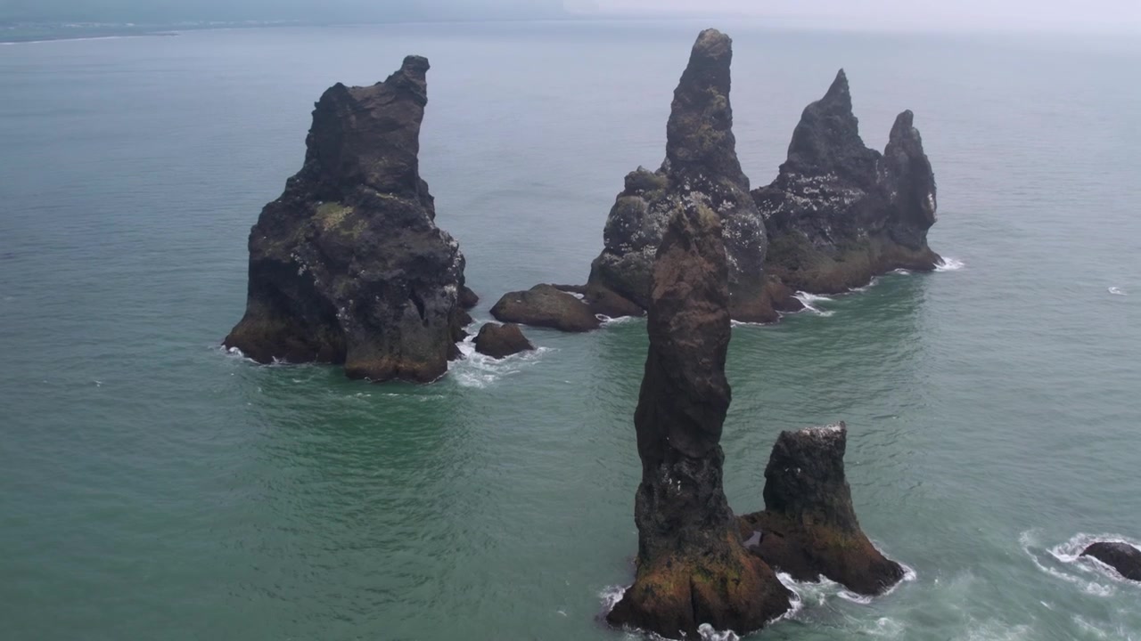 Majestátní letecký pohled na slavné čedičové útesy Reynisdrangar tyčící se ze Severního Atlantiku za mlhavého dne na jihu Islandu.