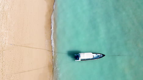 steady bird's view drone footage of sailing boat, fast boat in the blue ocean on the coast, beautiful yellow sand and waves moving the boat