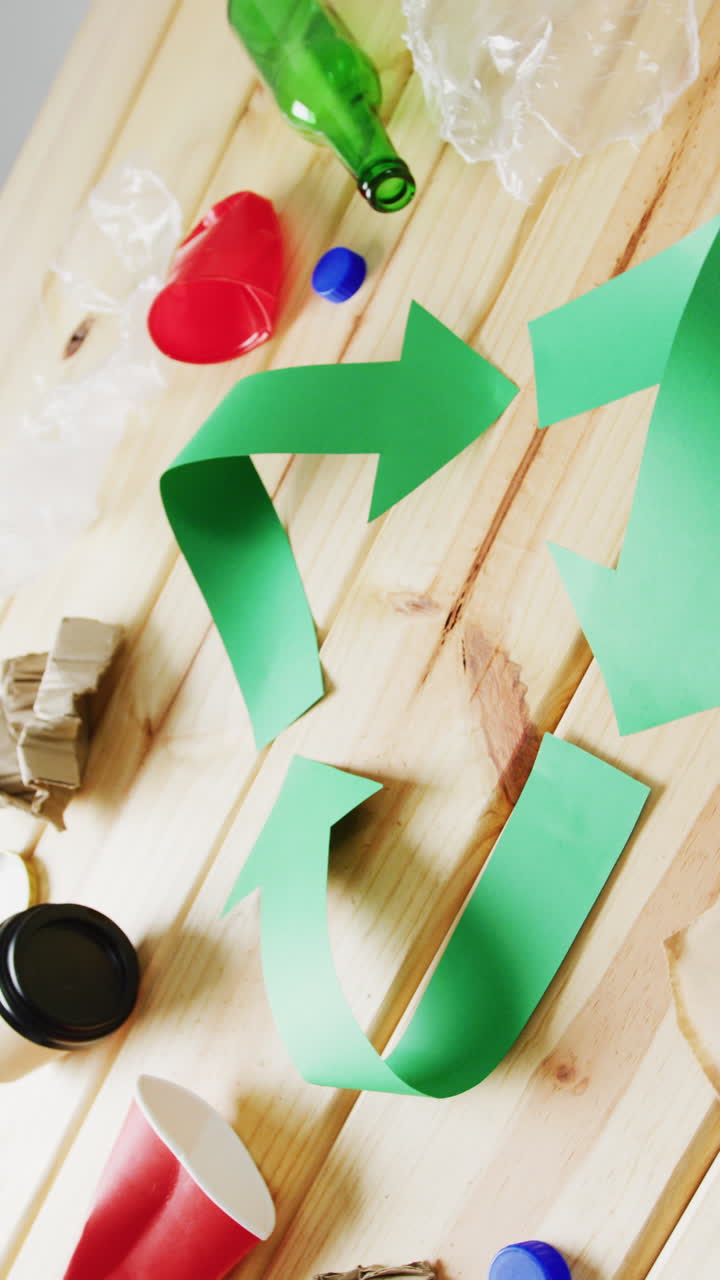 Vertical video of trash and recycling symbol of green arrows with copy space on wooden background