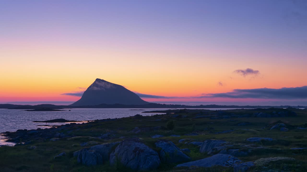 Siluet pulau pegunungan saat fajar dalam cahaya matahari terbit oranye-merah yang jernih. Awan tipis dan kabut laut muncul dan menghilang. Selang waktu. Lofoten, Norwegia Utara.