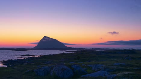 silhouette of a mountain island at dawn in the clear orange-red sunrise light. light clouds and sea mist appearing and disappearing. time lapse. lofoten, northern norway