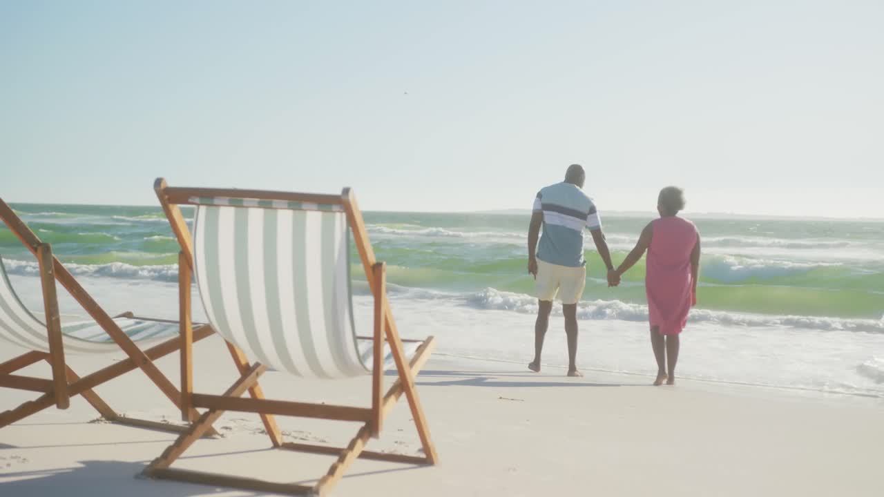 feliz pareja afroamericana de alto nivel caminando y tomados de la mano en la playa, en cámara lenta