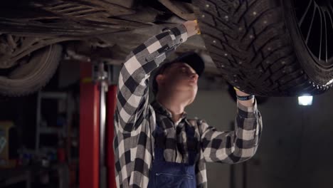 Gutaussehender-Mechaniker,-Der-In-Seiner-Werkstatt-Ein-Auto-Von-Unten-Repariert.