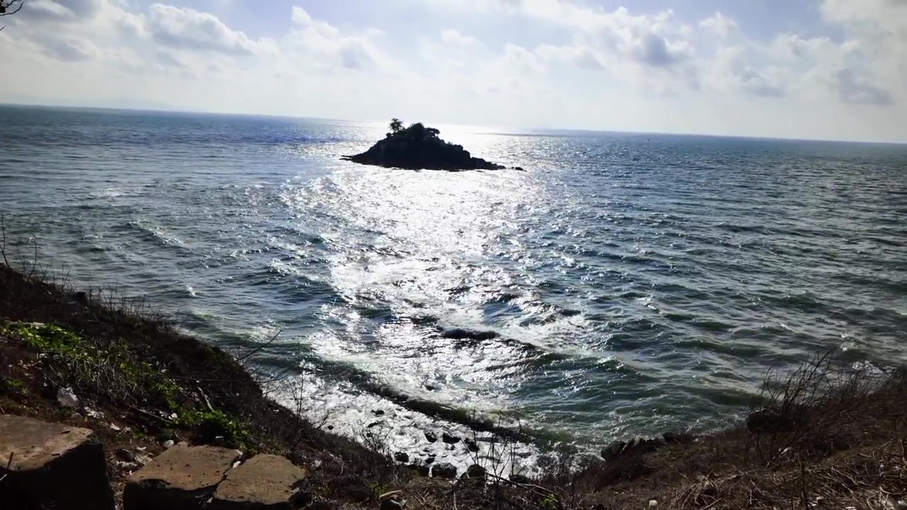 Folk besøker Nginh Phong-parken i Vung Tau, Vietnam. De nyter havutsikten og den lille øya i det fjerne. Bølgene kruser seg i vannet under den lyse himmelen.
