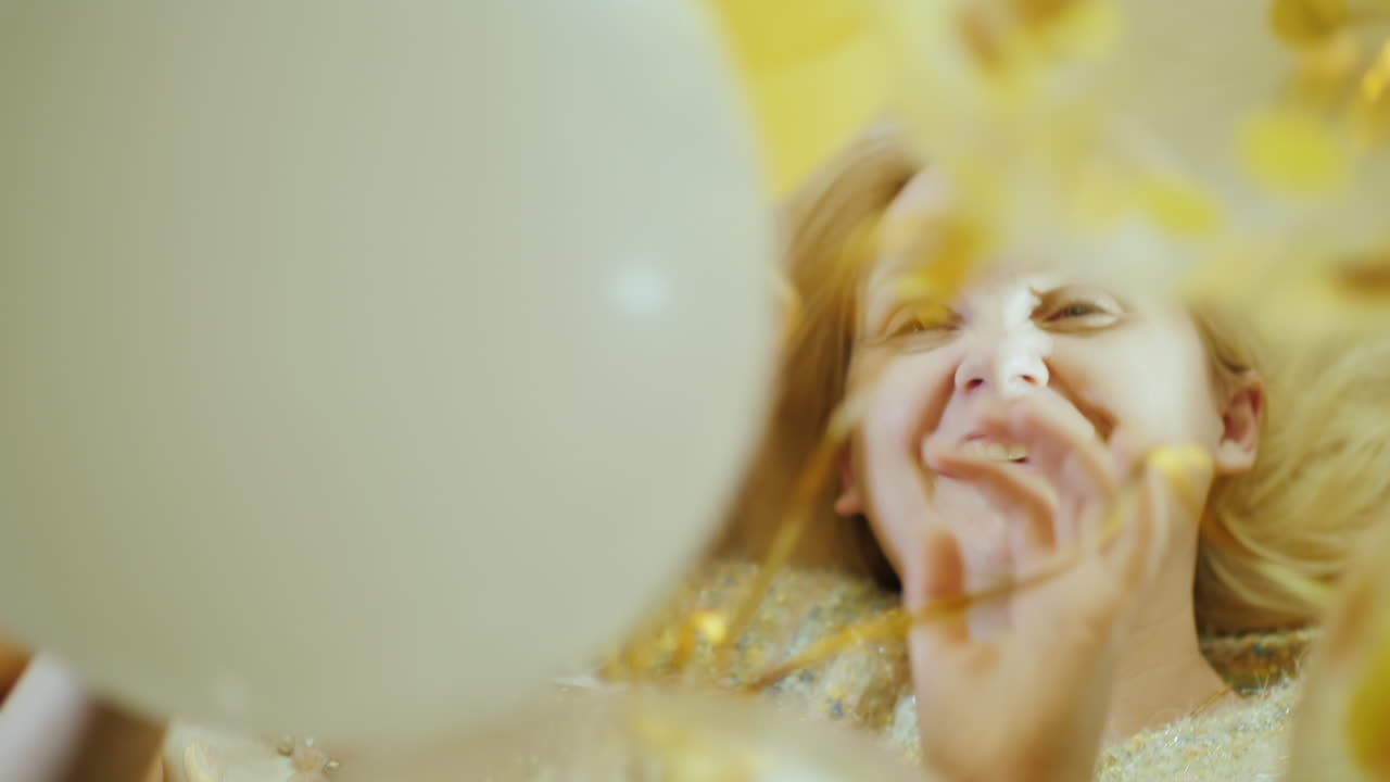 한 소녀와 그녀의 어머니가 웃으며 풍선을 가지고 놀고 있습니다. 그들은 침대 머리에 나란히 누워 있습니다.