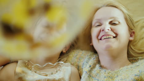 a girl and her mother are playing with balloons laughing they lie side by side on the bed head to he