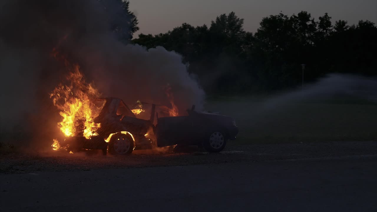 Burning car in the evening hours is extinguished with water from the right - enormous smoke development - Slow Motion