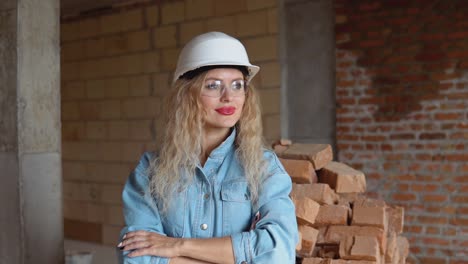 a young woman in a work helmet and denim clothes and goggles stands at the construction site. monitoring of safety at the construction site
