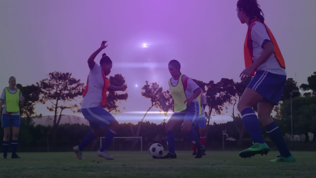 Five women soccer team practicing dribbling in bibs at dusk with animated sports training overlay